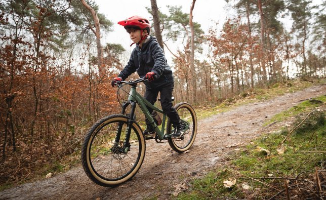 Un garçon descend un chemin forestier sur un vélo SUPURB avec fourche à suspension. 