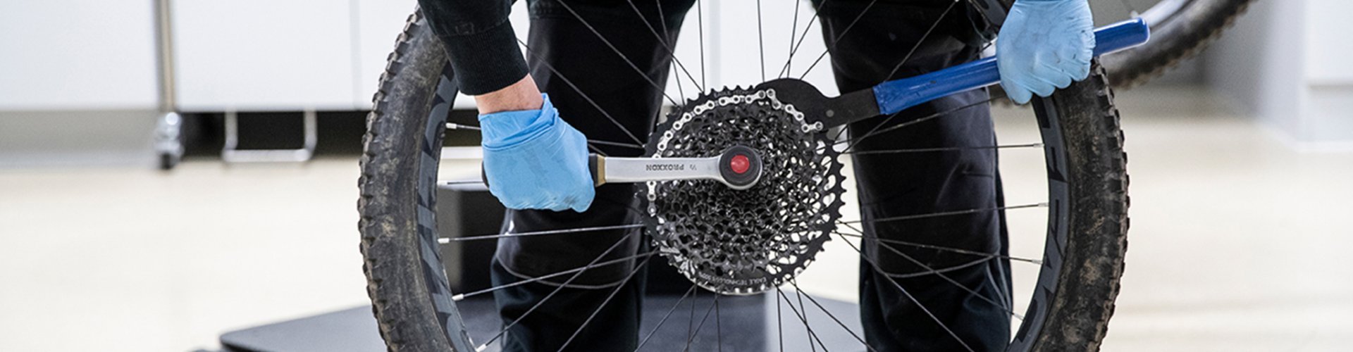 A chain whip and cassette removal tool are attached to the cassette. The cassette is loosened by the mechanic.