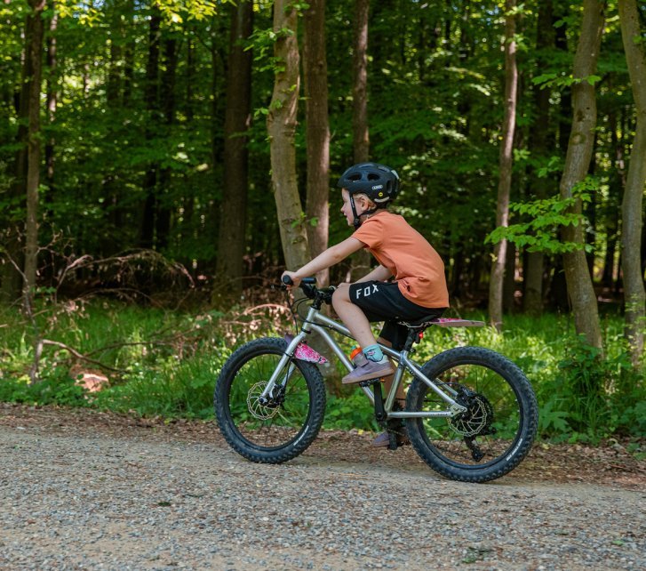 A girl rides an Early Rider through the forest. Her bike also has fenders and lighting.