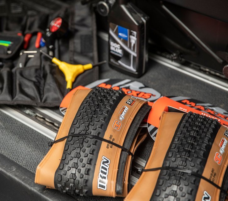 Une paire de pneus VTT Maxxis Ikon 29" est prête à être montée. En arrière-plan, on peut voir des outils pour pneus adaptés et du fluide d'étanchéité.