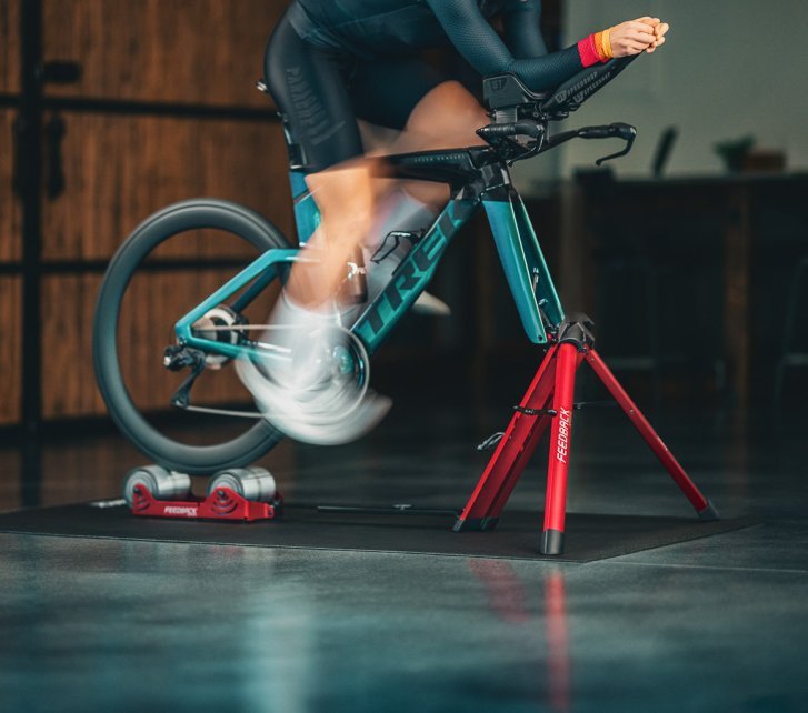 A person trains with a sea-green Trek road bike on a red Feedback Omnium roller trainer.