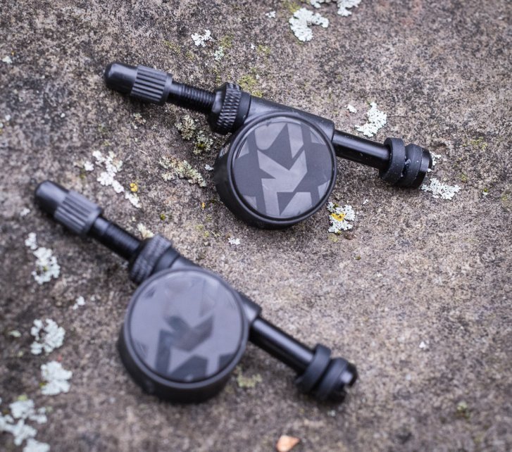 Zwei SKS Airspy Tubeless-Ventile mit integriertem Luftdruckprüfer liegen auf einem flechtenbewachsenen Naturstein. 