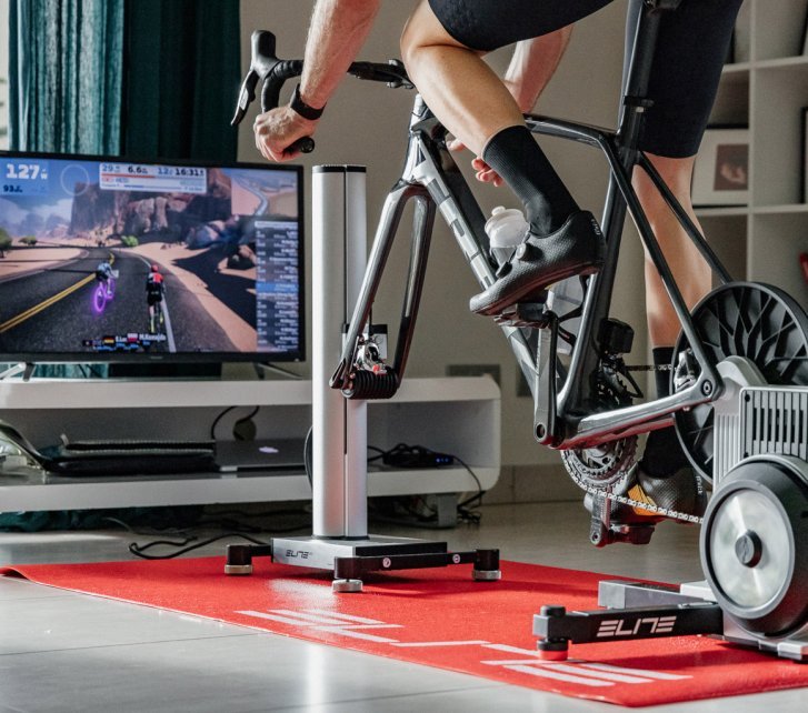 Una persona entrena en un smart trainer de Elite frente a un televisor en un salón.