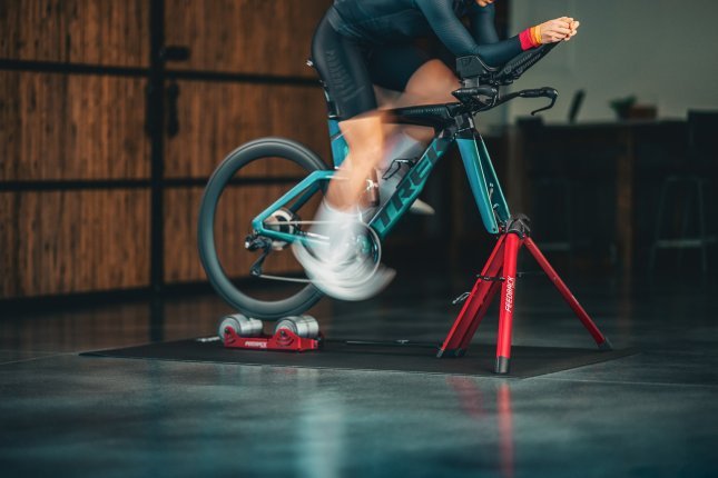 A person trains with a sea-green Trek road bike on a red Feedback Omnium roller trainer.