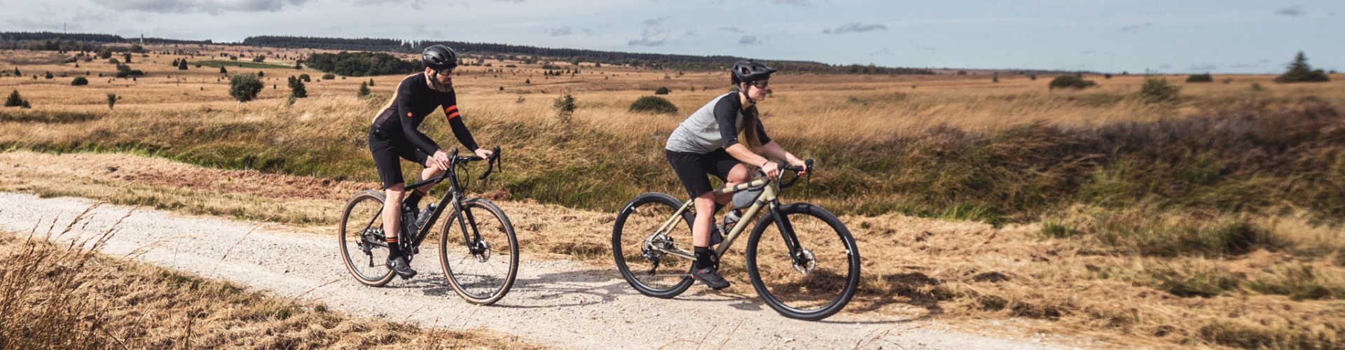 Ein Mann und eine Frau fahren mit ihren Gravelbikes durch eine Feldlandschaft.