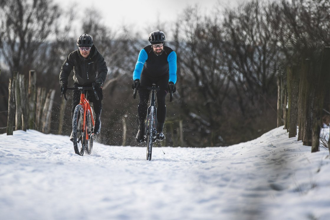 Dos hombres en gravel bikes rodando hacia la cámara en un paisaje nevado.