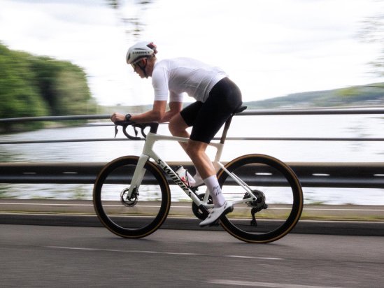 Rennradfahrer auf einem weißen S-Works Tarmac SL9 fährt dynamisch entlang einer Straße am See.