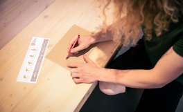 Two imprints on a piece of corrugated cardboard are being marked with a red pen.