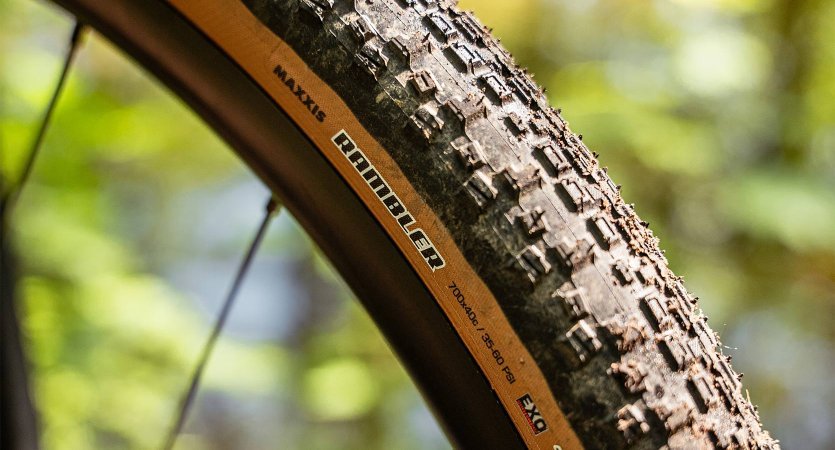 Gros plan d’un pneu gravel à crampons marqués et flanc beige, monté à l’avant du vélo.