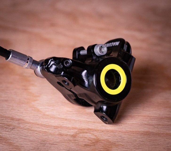 Una pinza de freno Magura negra con un aro amarillo brillante reposa sobre una tabla de madera.