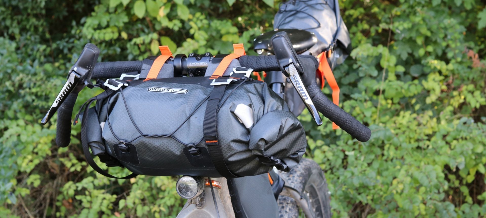 Ein Fahrrad mit einer Ortlieb Handlebar-Pack-Tasche, die am Lenker befestigt ist, vor einem Hintergrund von grünem Gebüsch.