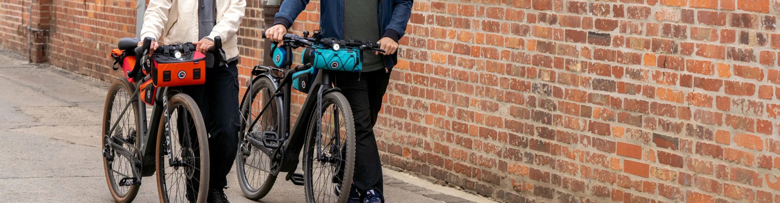 Zwei urbane Radfahrer mit Fahrradhelmen schieben ihre City-Bikes durch eine Backsteinstraße; Lenkertaschen von Contec unterstreichen alltagstaugliches Urban-Cycling und Pendler-Mobilität.