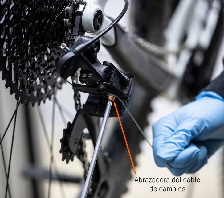 Mientras el mecánico de bc aprieta el tornillo de sujeción con una llave hexagonal, tira del cable de cambios con la otra mano.