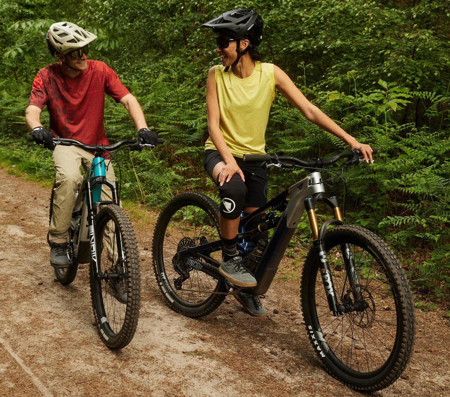 Two mountain bikers wearing Endura apparel and helmets riding relaxed on a forest trail while talking during their ride on mountain bikes.