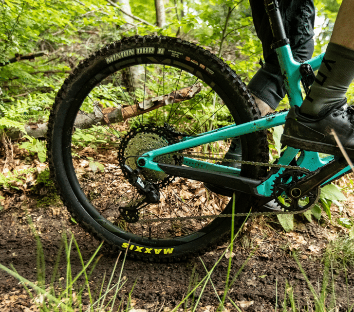 A mountain biker rides a Santa Cruz through the forest. The focus of the photo is on the bike’s rear triangle.