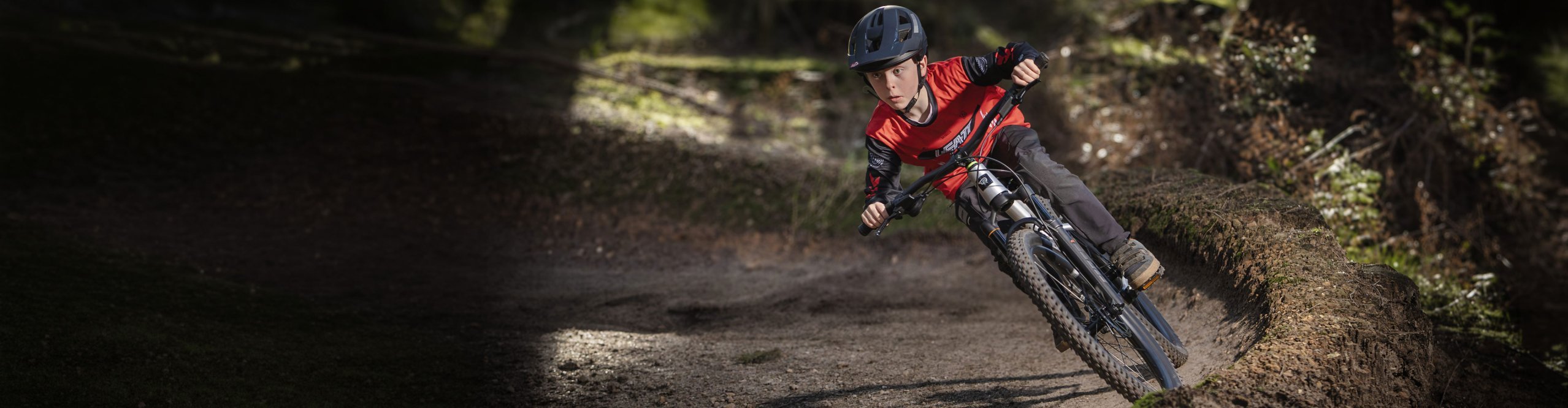 Kind fährt mit einem Early Rider Kinder Mountainbike dynamisch durch eine Waldkurve auf dem Trail