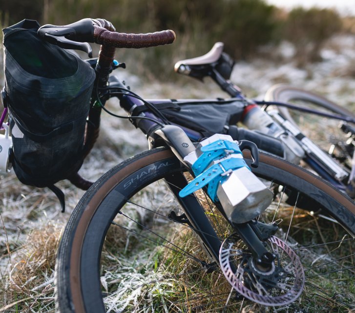 A gravel bike lies in the frost-covered grass. An espresso maker is strapped to the fork. 