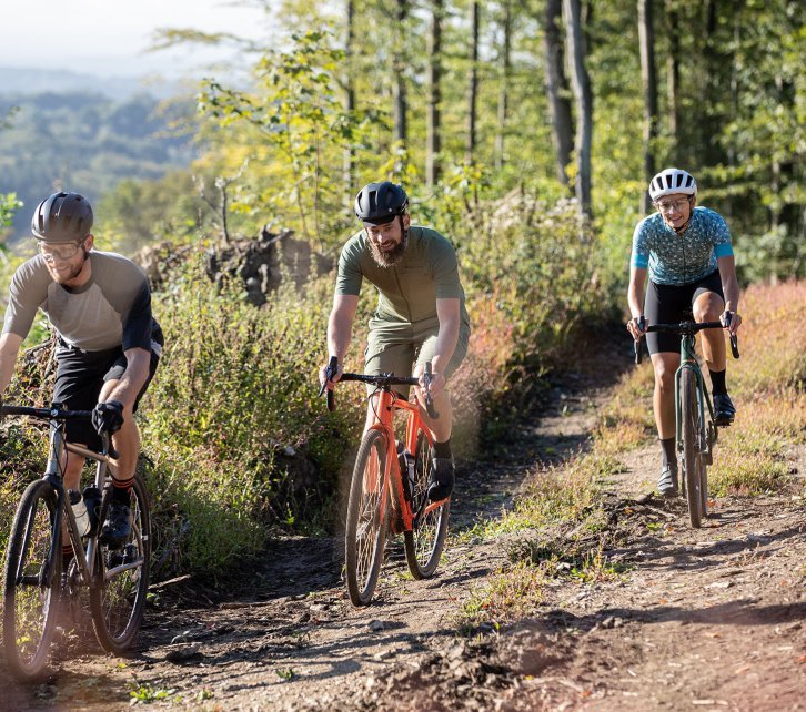 Markus, Björn et Anne de l'équipe bc roulent sur des gravelbikes sur un chemin forestier. 