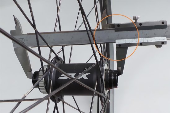 A caliper is applied to a front hub. The scale shows an installation width of 100 mm.
