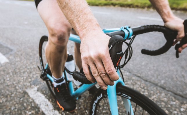 Un ciclista de ruta va con las manos posicionadas en las manetas de frenos mientras frena. 