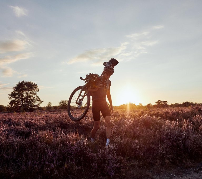 Graveler trägt sein Bike im Sonnenuntergang durch die Heide