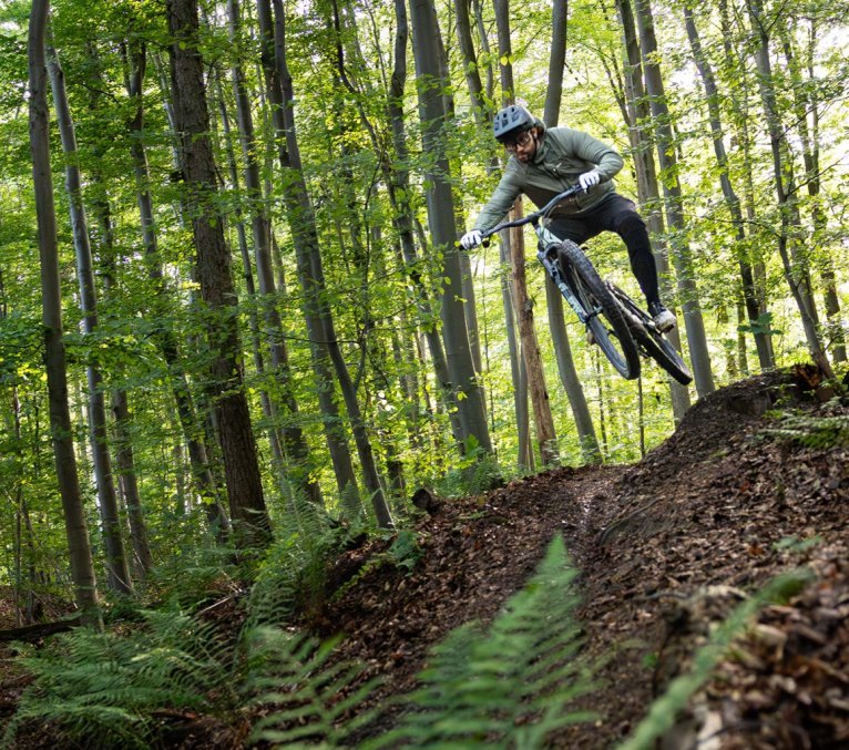 Berno springt mit dem Specialized Turbo Levo R von einem kleinen Kicker im Wald ab.