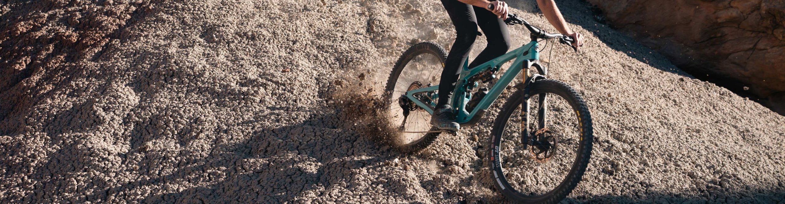 Actionfoto: Mountainbiker mit türkisfarbenem Yeti Mountainbike rutscht über groben Schotterhang, Staubwolke.