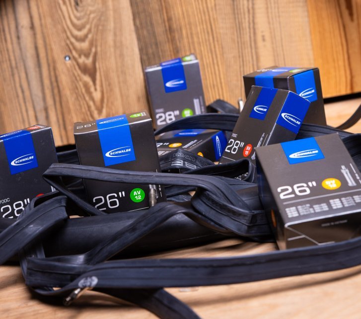 Some empty black rubber bicycle tubes lie tangled on a wooden surface. In between are grey-silver Schwalbe boxes containing tubes.