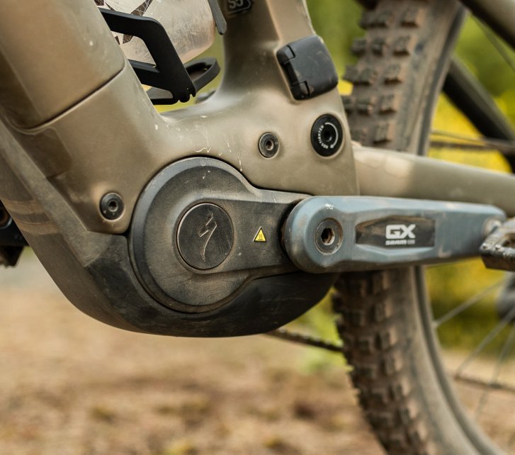 Detailfoto vom Tretlager- und Motorbereich eines bronze-grünen Specialized Turbo Levo 4 im Wald. 