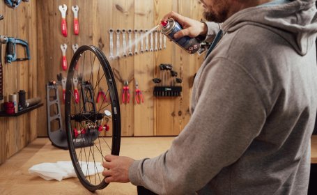 Person reinigt eine Fahrradfelge in der Werkstatt mit Bremsenreiniger aus einer Sprühdose, Vorbereitung für das Anbringen von Felgenband.