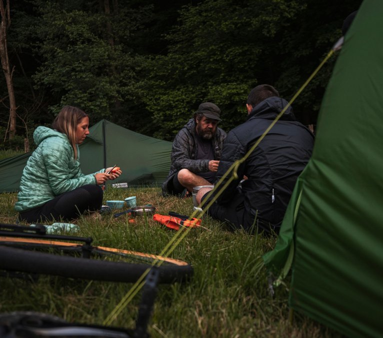 3 bc Mitarbeiter sitzen vor ihren Zelten und bereiten das Abendessen vor.