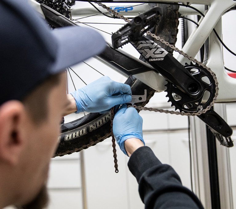 A chain whip and cassette removal tool are attached to the cassette. The cassette is loosened by the mechanic.