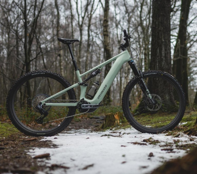 Nouveau VTT électrique Specialized Turbo Levo R tout-suspendu vert menthe, vue de profil sur un sentier en forêt