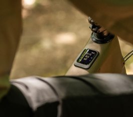 Display of a Specialized Turbo Levo 4 E-MTB photographed from behind at an angle. Blurred torso, thigh and arm of the rider frame the image in the foreground