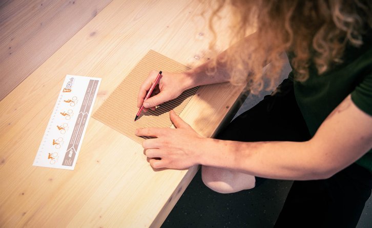 Two imprints on a piece of corrugated cardboard are being marked with a red pen.