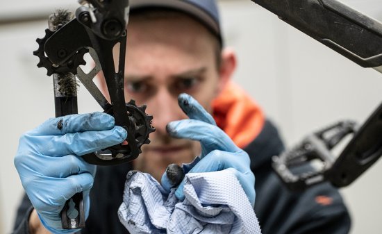 bc-Mechaniker Thomas reinigt das untere Schaltröllchen des Schaltwerks mit einem blauen Papiertuch.