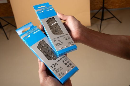 Zwei Shimano Fahrradketten in Verpackung werden in den Händen gehalten und zeigen den Unterschied zwischen 11-fach und 12-fach.