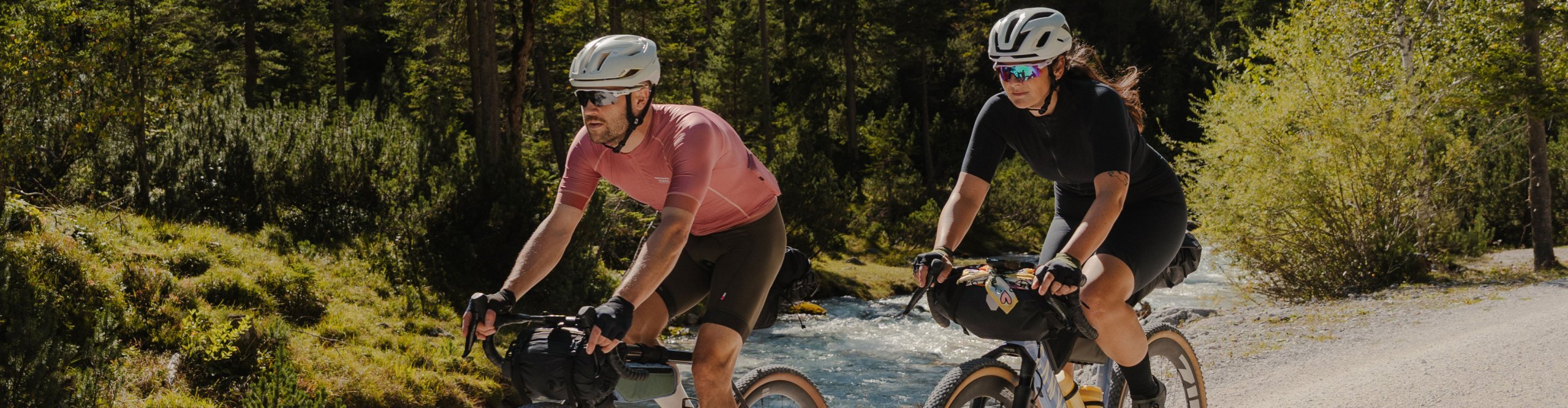 Two gravel bikepackers ride along a riverside forest trail wearing Roeckl Sports cycling gloves.
