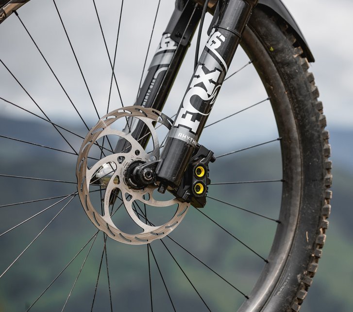 Front wheel of a mountain bike with disc brake and FOX suspension fork, blurred landscape in the background.