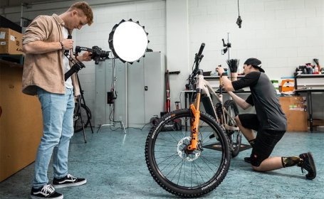 Fahrrad-Check in der Werkstatt: Mechaniker stellt Mountainbike ein, Fotograf dokumentiert den Service