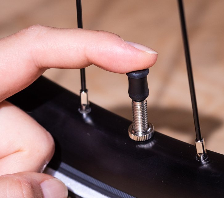 A finger presses a black cap onto a Schwalbe Clik Valve.