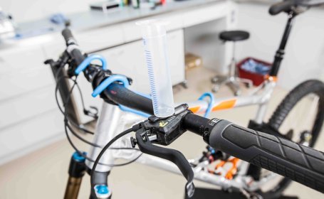 Eine leere Einwegspritze ohne Kolben ist stehend auf der Geberpumpe einer hydraulischen Fahrradbremse eingesteckt.