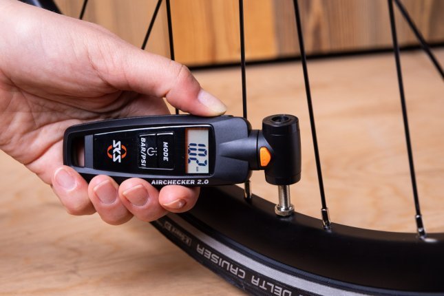Close-up photo: A woman's hand holds an SKS pressure gauge against a bicycle valve.