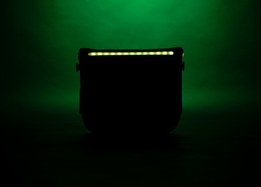 Eine schwarze ORTLIEB Lenkertasche mit grünen Akzenten steht allein. Sie hat ein beleuchtetes, perforiertes Design. Der Hintergrund ist dunkelgrün.
