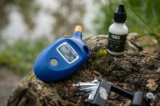 Medidor digital de presión de neumáticos y multiherramienta de bicicleta sobre un tronco en la naturaleza.