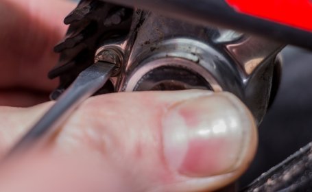 Gros plan d’un tournevis desserrant la vis de fixation d’un étrier de frein de vélo, avec un doigt stabilisant la zone.