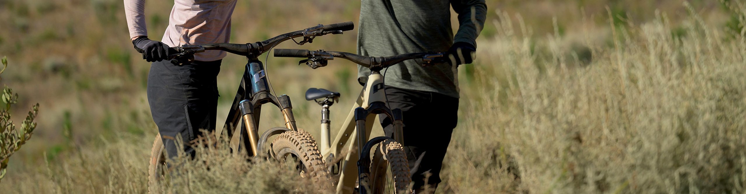 Dos ciclistas de montaña chocan las manos junto a sus MTB con manillares PRO en un sendero soleado.