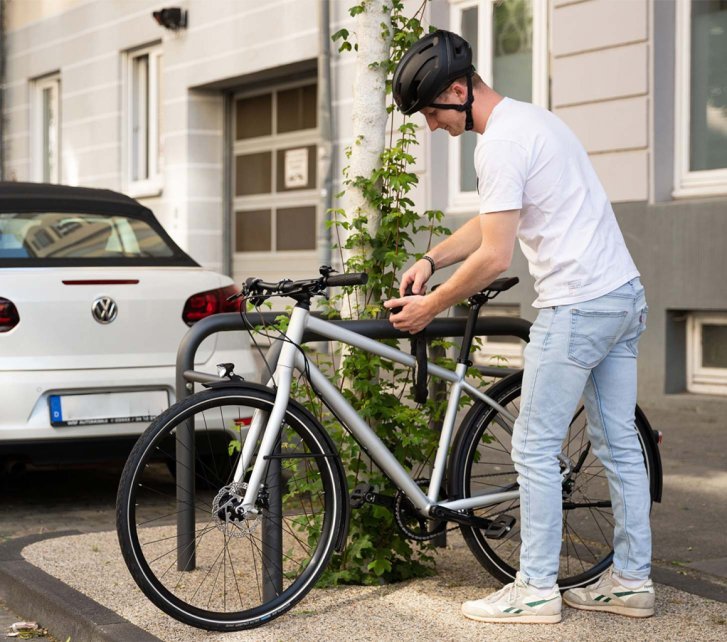Hombre con casco asegurando su bicicleta con un candado de cadena a un soporte en la calle.
