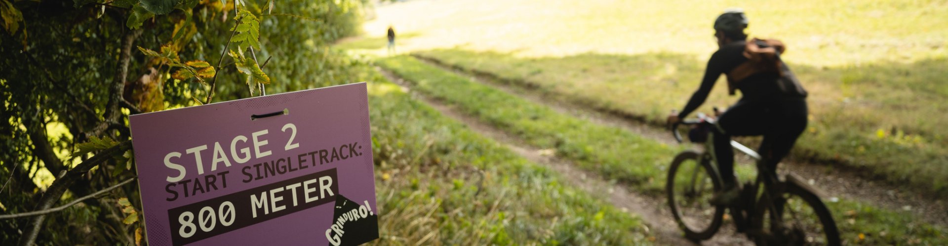 Auf der linken Seite des Waldwegs steht das Hinweis-Schild zur nächsten Stage des Grinduros. Ein Teilnehmer passiert diese Stelle.