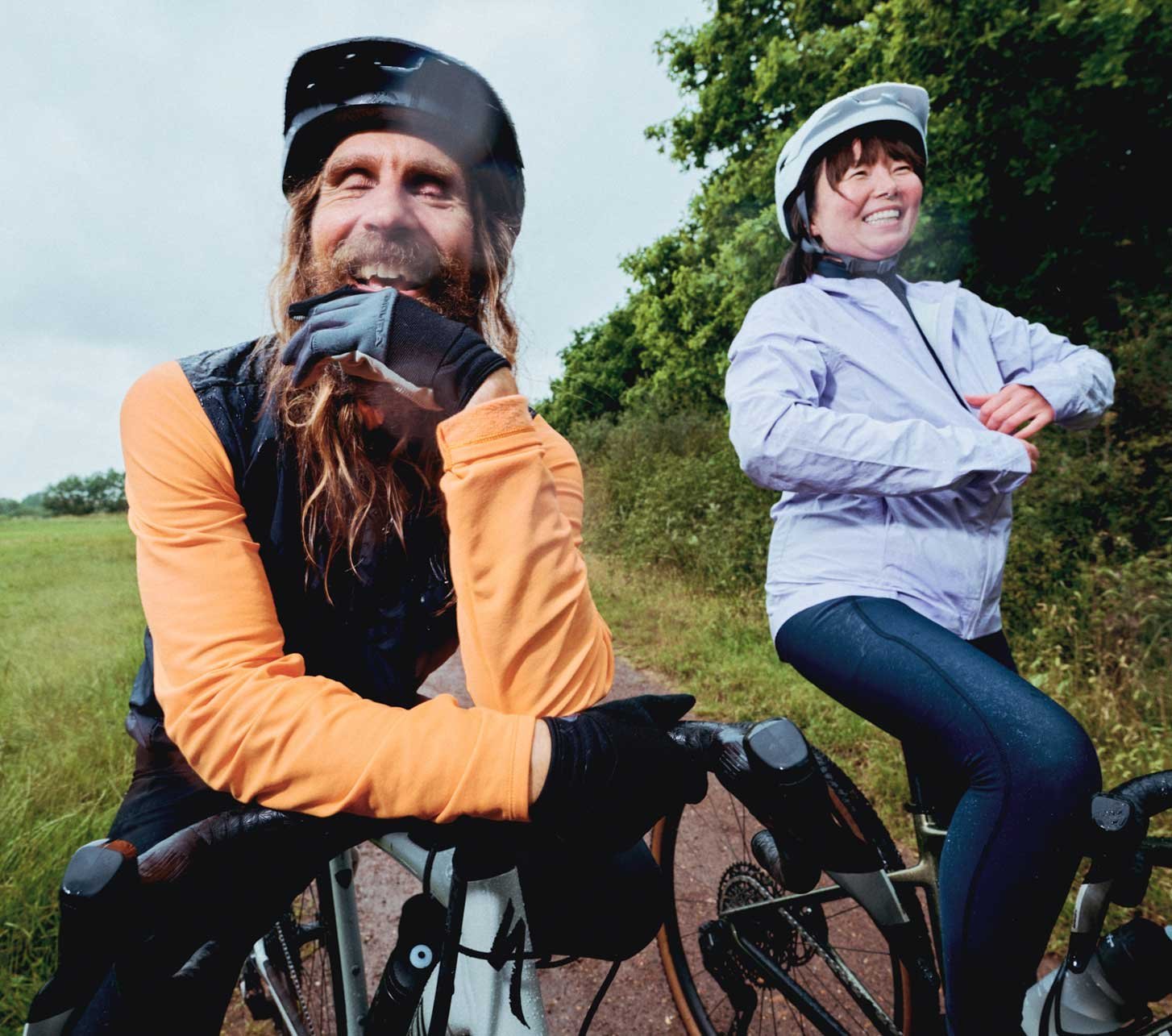 Two smiling cyclists wearing Endura rainwear taking a break on a country lane in wet weather.